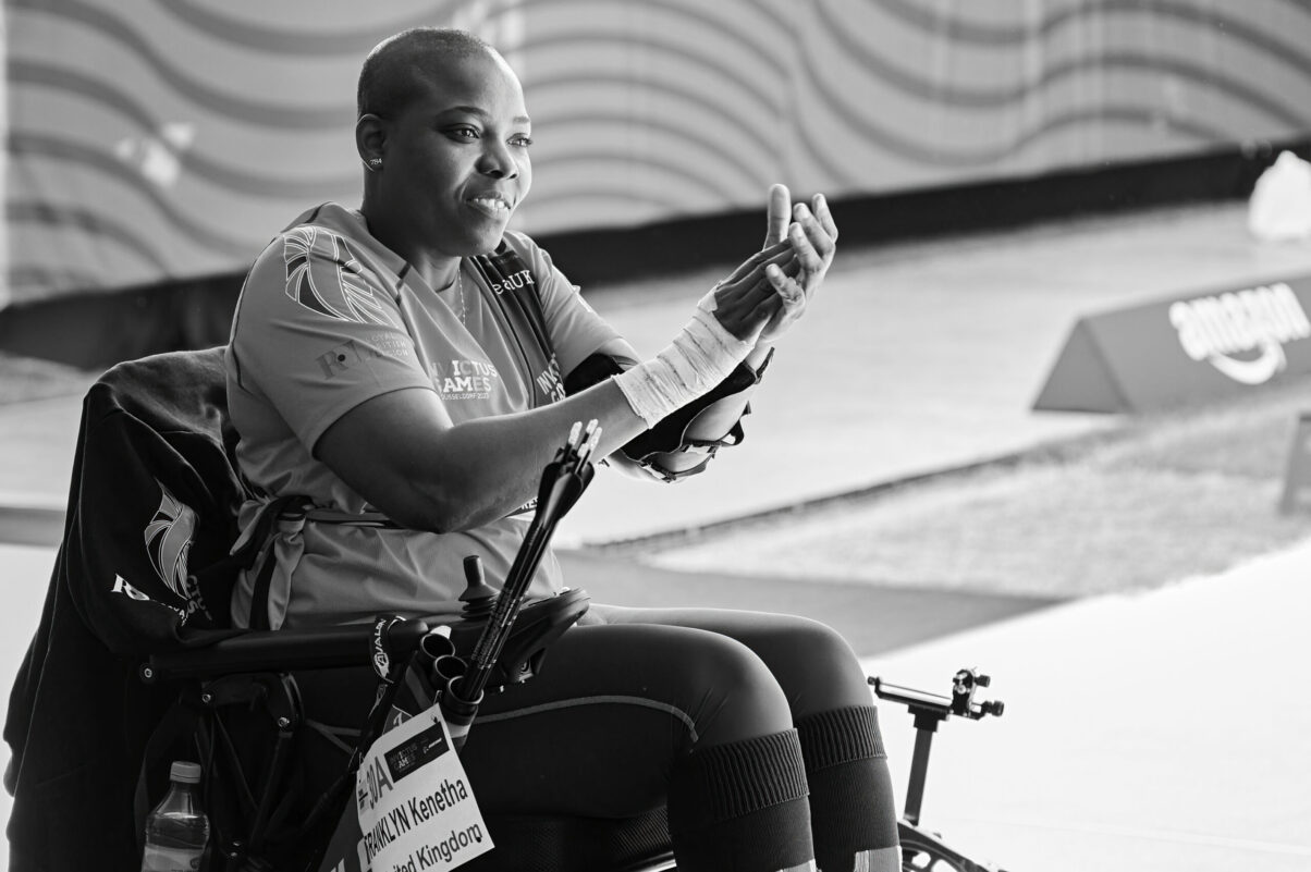 Ausstellung Spirit of Invictus Games Düsseldorf 2023 Bogenschützin im Rollstuhl einem anderen Sportler applaudierend