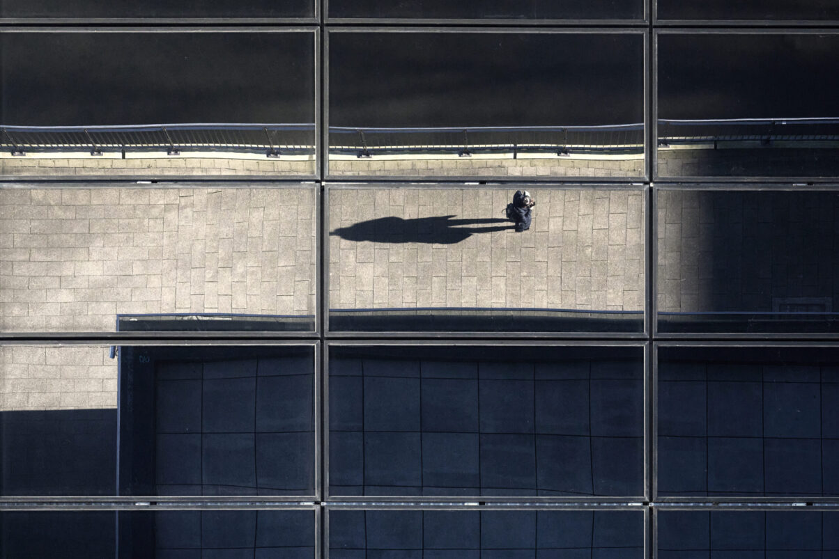 Blick nach unten durch ein Glasdach mit Eisenkonstruktion, unten eine Person im Sonnenlicht, Querformat