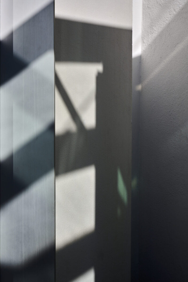 abstrakter minimalistischer Ausschnitt einer verschachtelten Hausfassade mit schrägen Schatten und Vertikalen, Hochformat