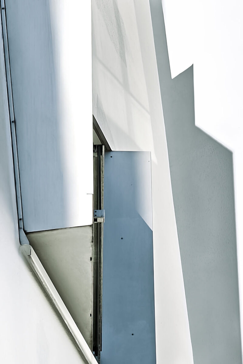 abstrakter minimalistischer Ausschnitt einer Hausfassade mit Fensteröffnung, Schattenspiel, Schrägen, Hochformat