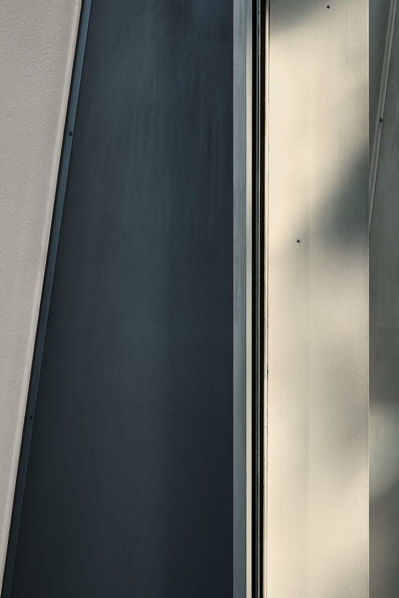 abstrakter minimalistischer Ausschnitt einer Hausfassade mit Schatten, Vertikale und wenig Schrägen, Hochformat