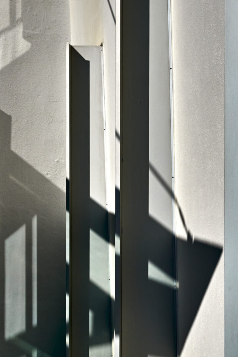 abstrakter minimalistischer Ausschnitt einer verschachtelten Hausfassade mit Schatten, Vertikale und Schrägen, Hochformat