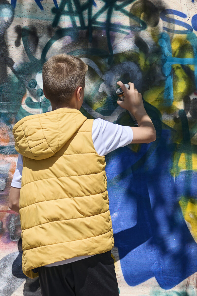 Eventfotografie Düsseldorf Sonnenrad Festival 2023 - Junge in gelber Weste mit Grafitti Sprühflasche beim Sprühen