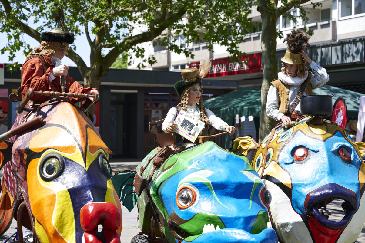 Eventfotografie Düsseldorf Sonnenrad Festival 2023 - altertümlich verkleidete Schausteller in fahrenden großen und bunten Fischen aus Pappmasche