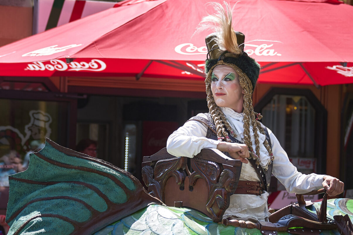 Eventfotografie Düsseldorf Sonnenrad Festival 2023 - Schausteller in barocker Kleidung mit Federhut und langen Zöpfen blickt in die Ferne