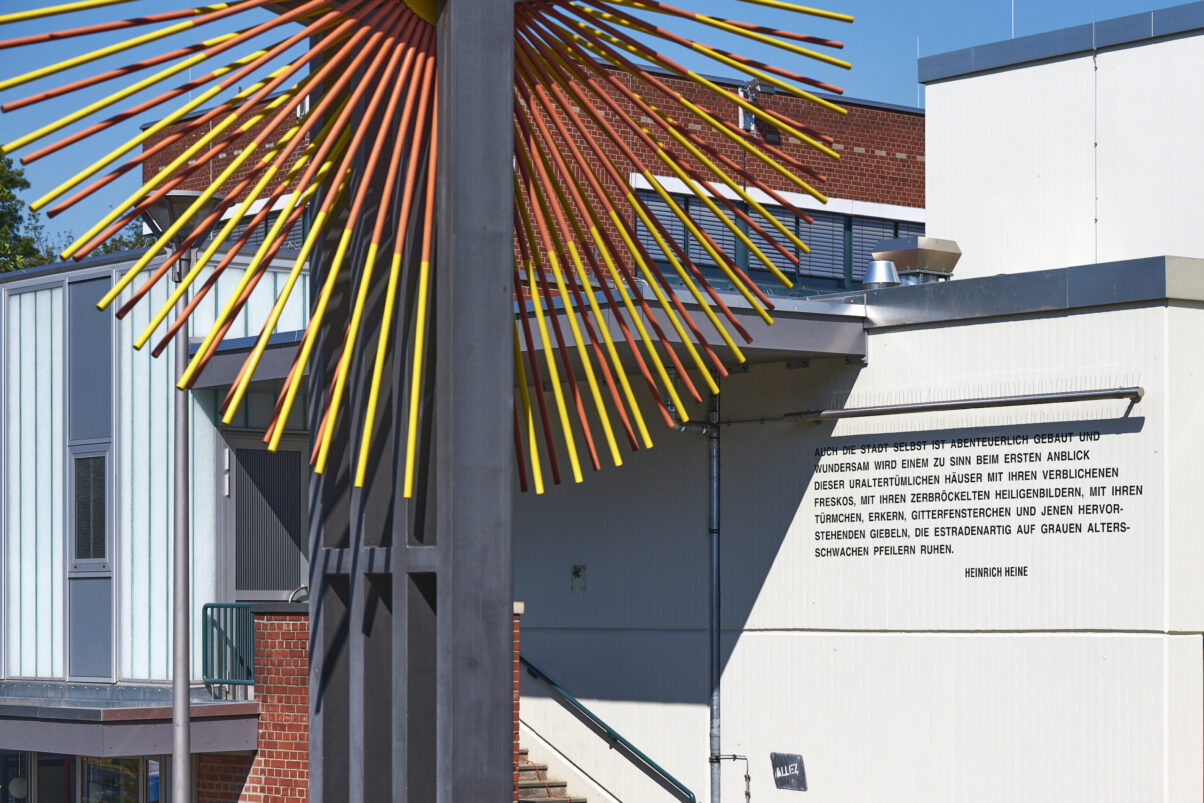 Eventfotografie Düsseldorf Sonnenrad Festival 2023 - Ausschnitt eines großen Windrades in Sonnenfarben vor weißer Wand mit Text von Heinrich Heine