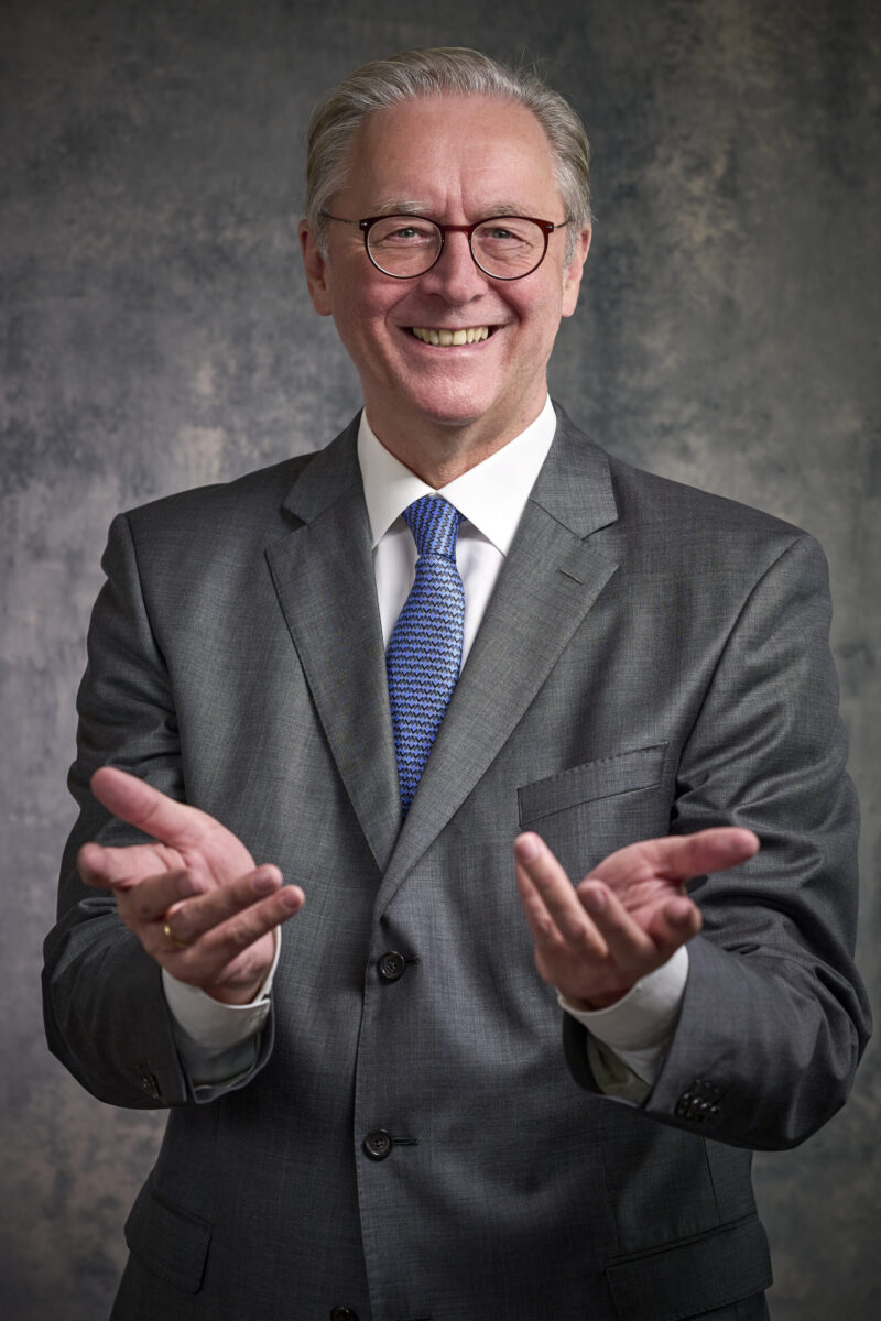 Peoplefotografie Düsseldorf, Business Porträts Düsseldorf Business Porträt eines lachenden Vorstandsmitglieds im dunkelgrauen Anzug mit offener Handhaltung