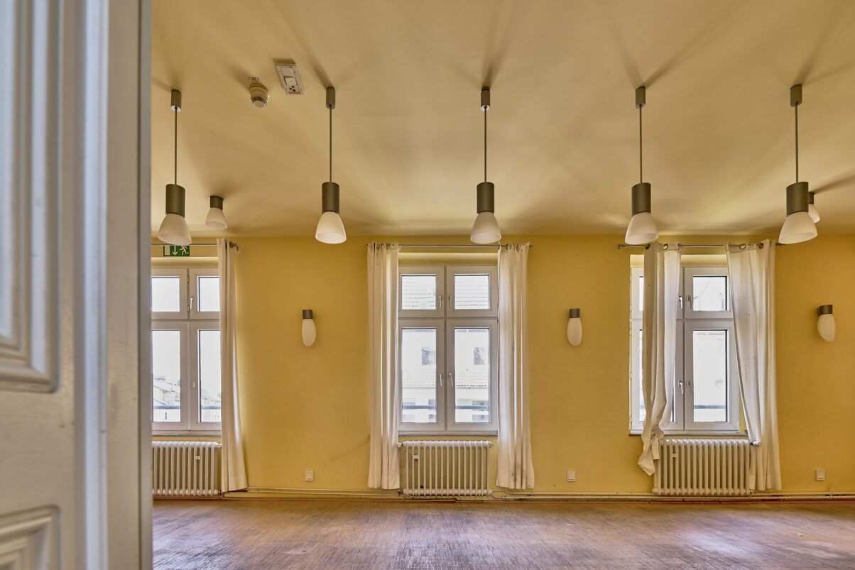 Architektur- und Interieurfotografie Düsseldorf SKFM Sanierung Altbau, großer prächtiger Raum in zwei Gelbtönen gestrichen, mit einer Vielzahl von Wand- und herabhängenden Deckenleuchten, Stäbchenparkett