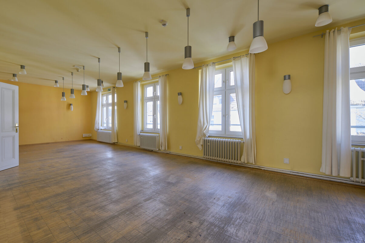 Architektur- und Interieurfotografie Düsseldorf SKFM Sanierung Altbau, großer prächtiger Raum in zwei Gelbtönen gestrichen, mit einer Vielzahl von Wand- und herabhängenden Deckenleuchten, Stäbchenparkett