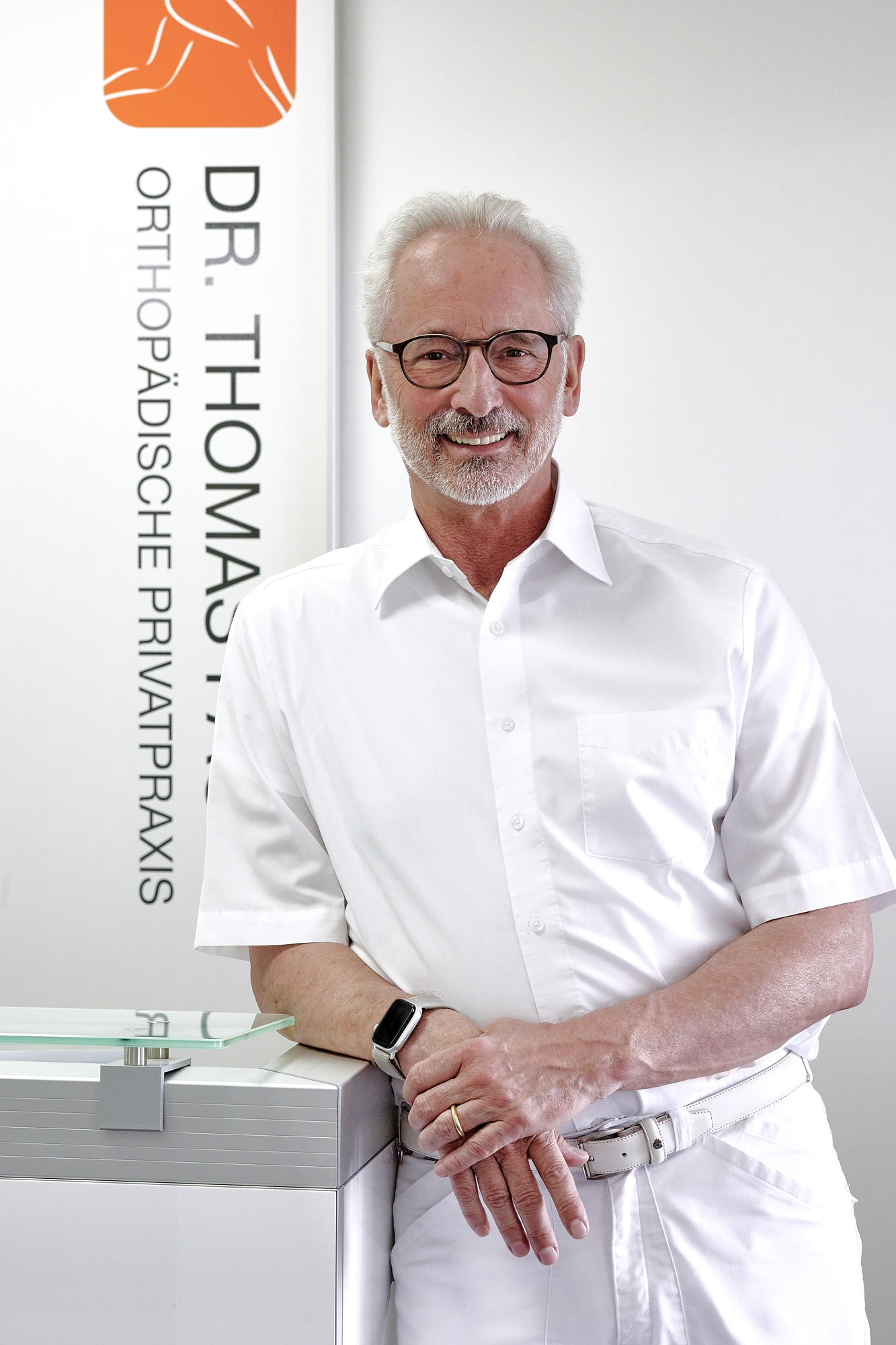 Peoplefotografie Düsseldorf, Business Porträts Düsseldorf Halbporträt eines lachenden Arztes angelehnt am Empfangstresen seiner Praxis