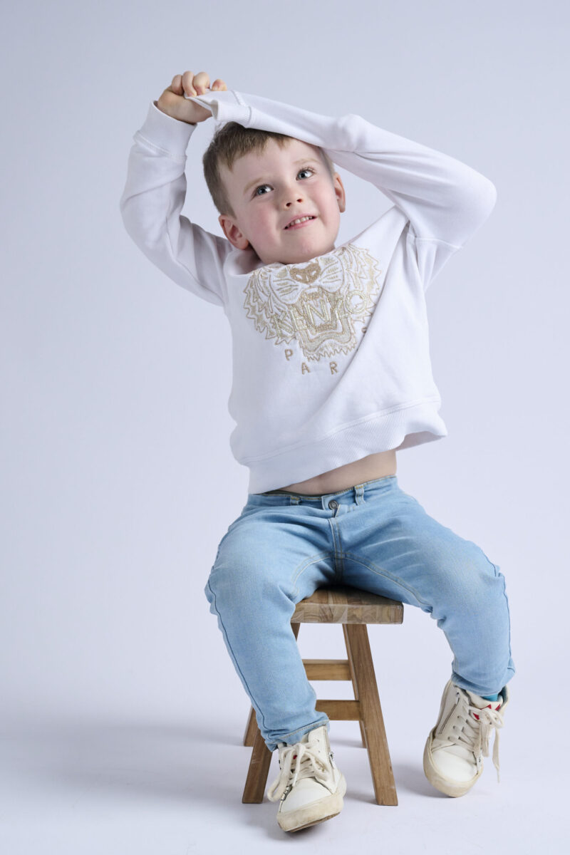 Kindershooting, Lachender kleiner blonder Junge auf Holzhocker