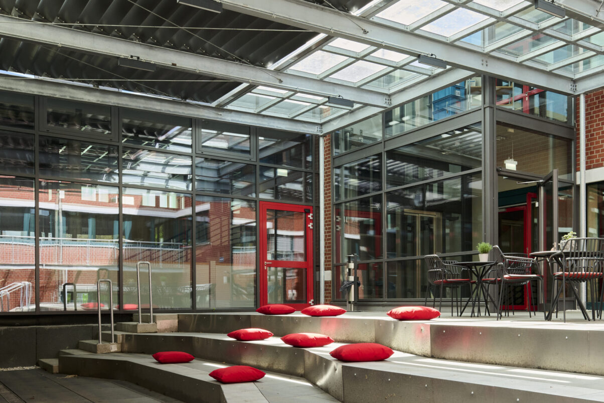 Architektur- und Interieurfotografie Düsseldorf Kulturhaus Süd, lichtdurchfluteter Innenhof, Freitreppe mit einigen roten Sitzkissen