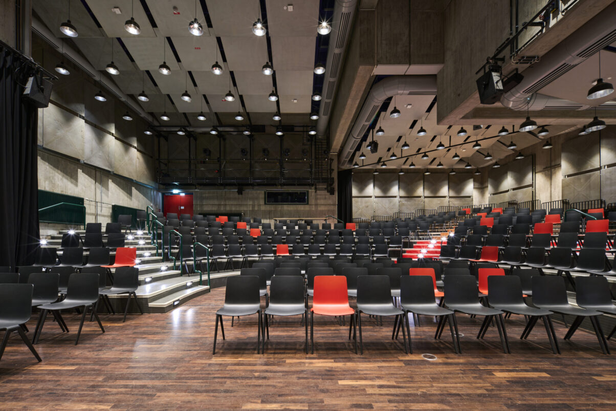 Architektur- und Interieurfotografie Düsseldorf Kulturhaus Süd, großer Festsaal mit überwiegend schwarzer und als Eyecatcher roter Bestuhlung und geöffnetem Vorhang zur rückwärtigen Raumerweiterung