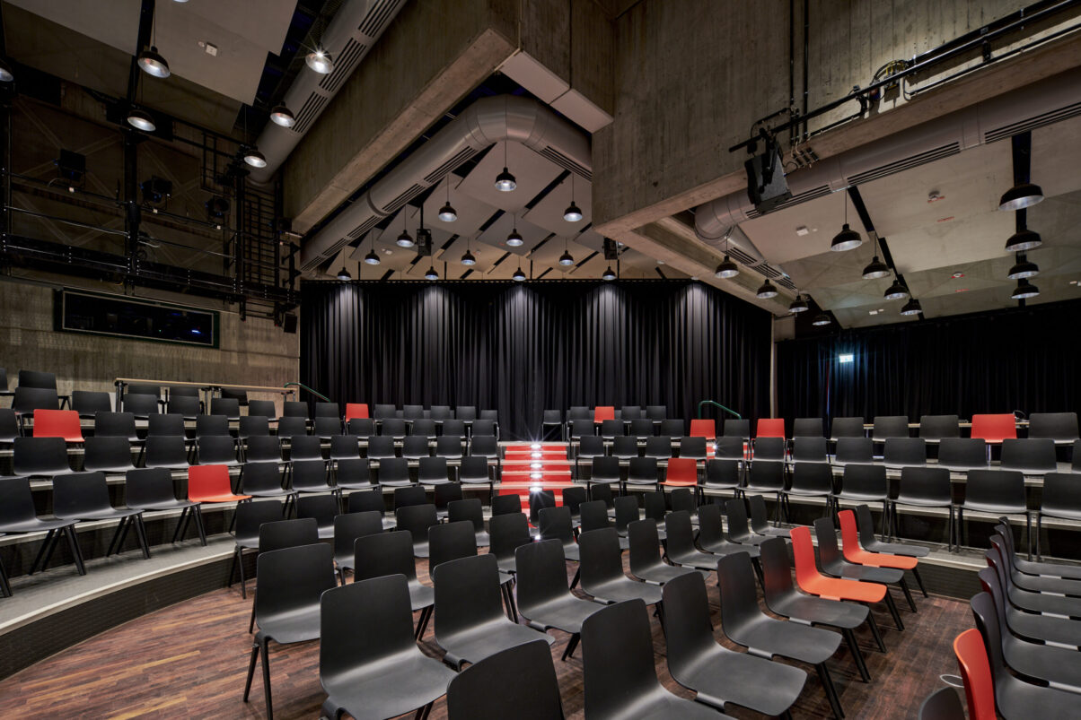Architektur- und Interieurfotografie Düsseldorf Kulturhaus Süd, großer Festsaal mit überwiegend schwarzer und als Eyecatcher roter Bestuhlung und durch Vorhang abgeteilte rückwärtige Raumerweiterung