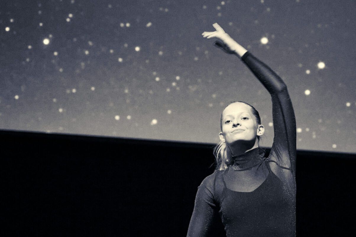 Eventfotografie Düsseldorf Ballettaufführung, eine Tänzerin in glitzerndem Rollkragen-Oberteil, moderne Choreographie, Sternenhimmel, Blautönung