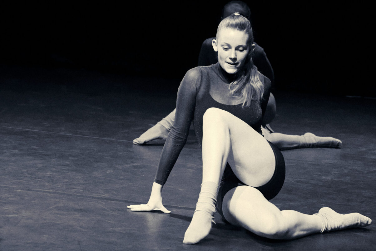 Eventfotografie Düsseldorf Ballettaufführung, moderne Choreographie, Tänzerin auf dem Boden posierend im sportlichen Look mit glitzerndem Rollkragen-Oberteil, Sternenhimmel, Blautönung