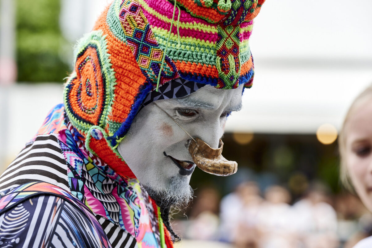 Pop up Artistik Festival, farbenprächtig gekleideter Pantomime Clown, lächelnd im Dialog