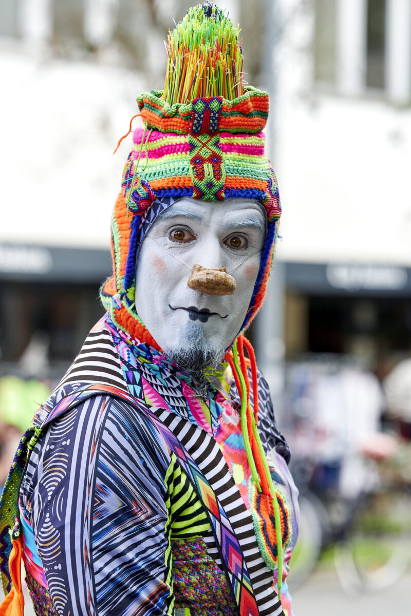 Pop up Artistik Festival, farbenprächtig gekleideter Pantomime Clown, mit großen Augen in die Kamera schauend