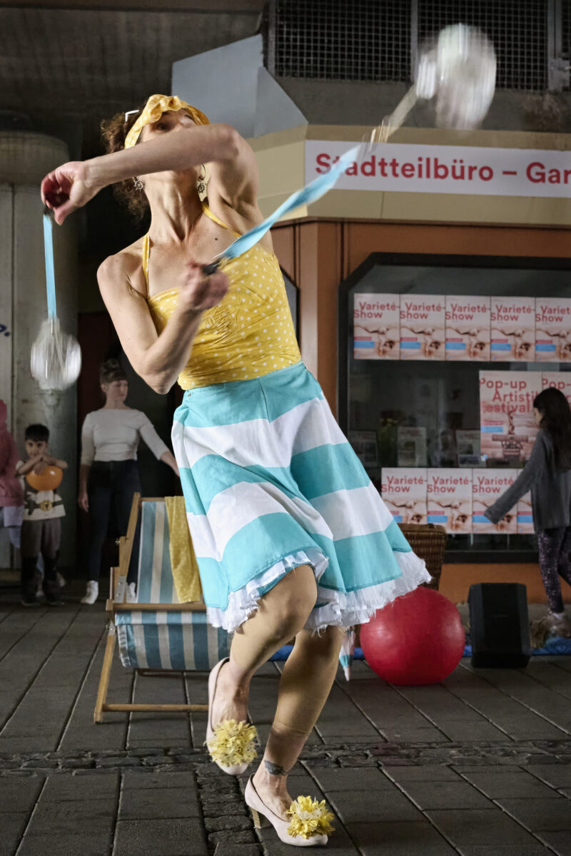 Pop up Artistik Festival, Artistin, zwei mit Wasser gefüllte Glasgefäße an Bändern jonglierend
