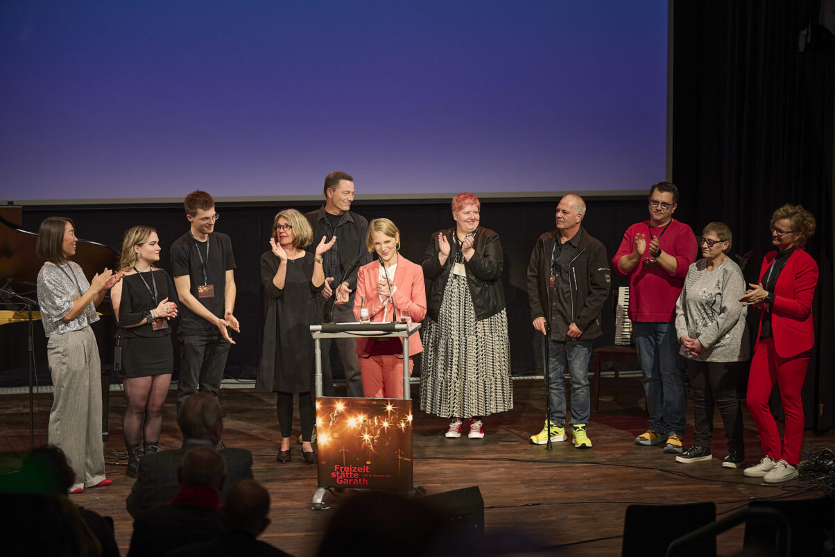 Eröffnungsgala Kulturhaus Süd - Mitarbeiter stehen im Kreis auf der Bühne und gratulieren der Leiterin des Kulturhauses Süd.