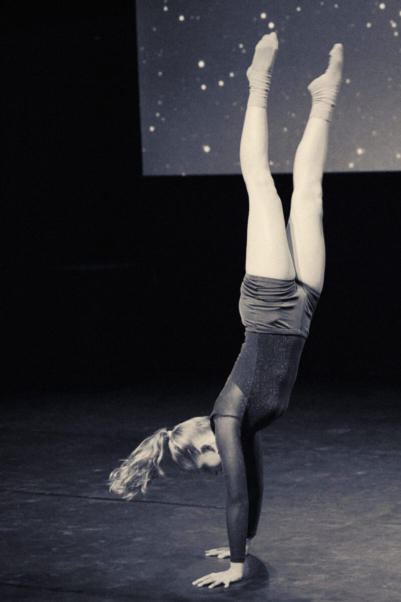 Eventfotografie Düsseldorf Ballettaufführung, moderne Choreographie, Tänzerin im Handstand im sportlichen Look mit glitzerndem Rollkragen-Oberteil, Sternenhimmel, Blautönung