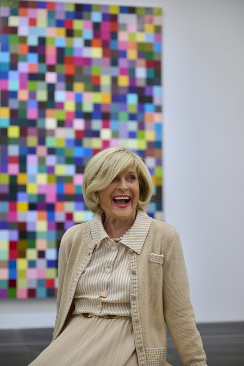 Ältere gut gestylte und herzhaft lachende Dame im Museum. Im Hintergrund ein Mosaikgemälde von Gerhard Richter