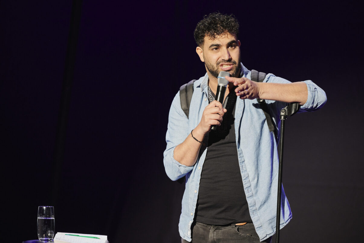 Eröffnungsgala Kulturhaus Süd - Comedian im hellblauen Jeanshemd spricht ins Mikrofon und schaut ins Publikum