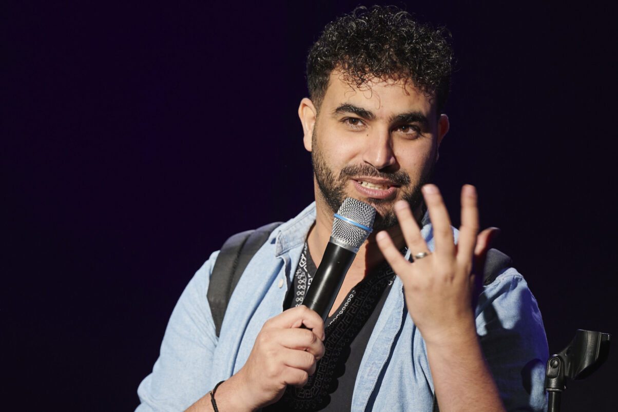 Eröffnungsgala Kulturhaus Süd - Comedian im hellblauen Jeanshemd spricht ins Mikrofon und schaut ins nach vorne