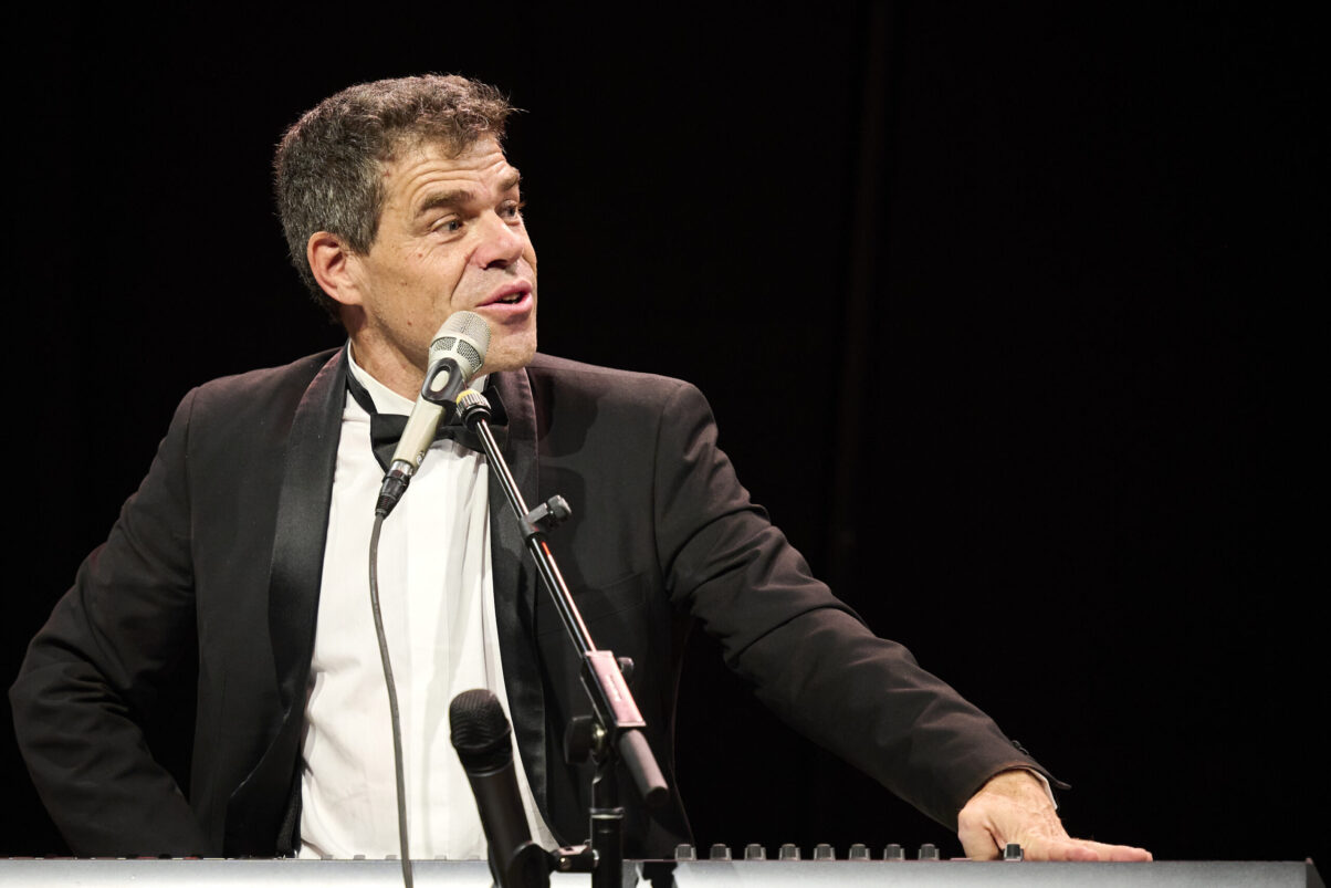 Eröffnungsgala Kulturhaus Süd - Comedian im schwarzen Smoking auf der Bühne am Keyboard schaut ins Publikum