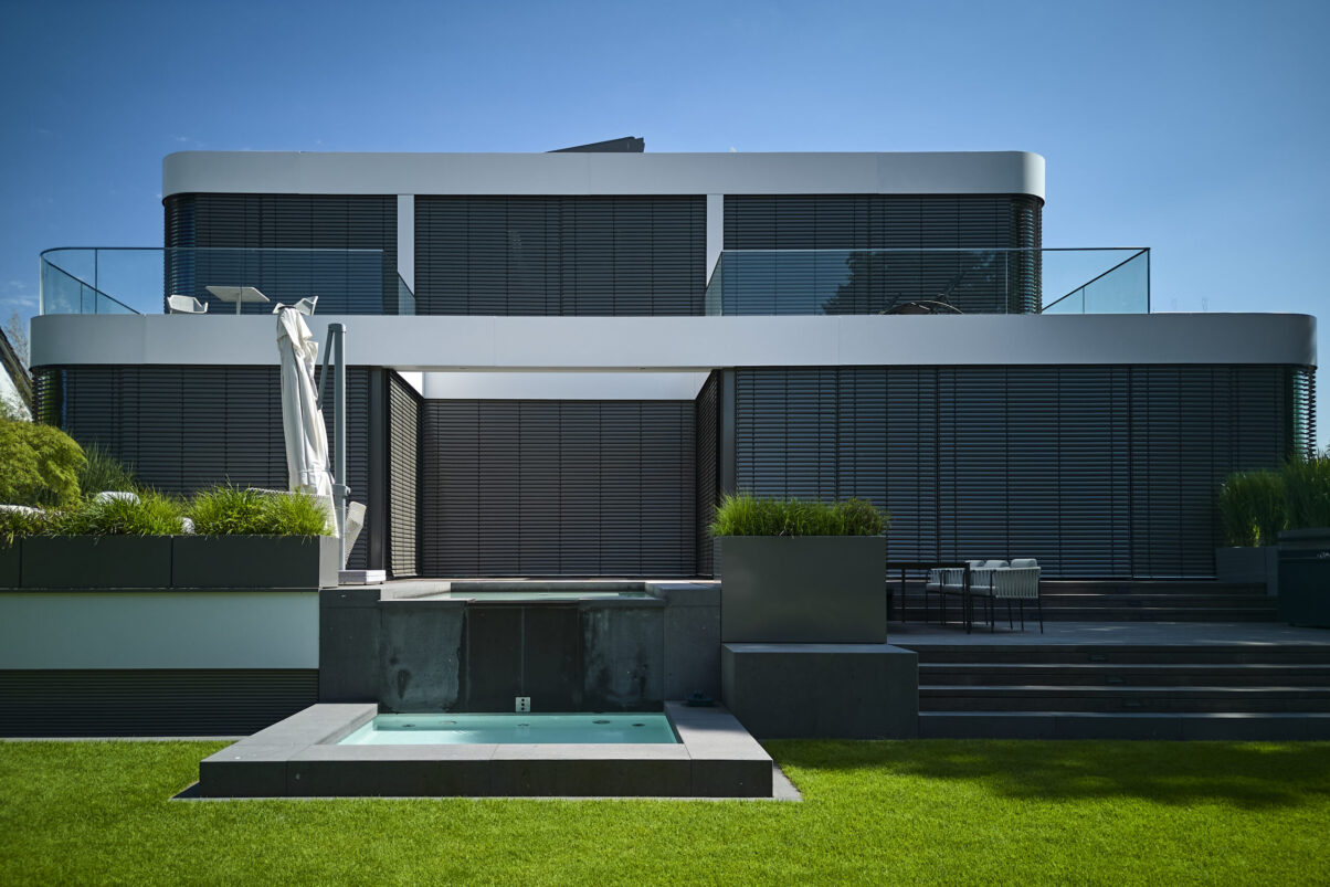 Architektur- und Interieurfotografie Düsseldorf MH Project, Gartenansicht des futuristischen Hauses mit geschlossenen Aussenjalousien, davor ein moderner zweistufiger Brunnen