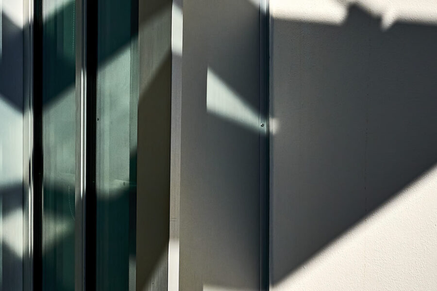 abstrakter minimalistischer Ausschnitt einer Hausfassade mit Schatten, Vertikale und Schrägen, Querformat