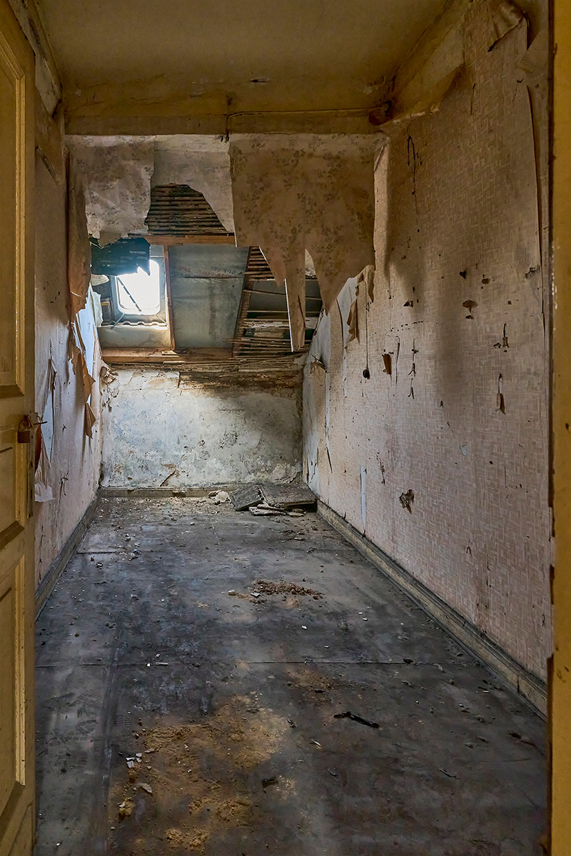 Architektur- und Interieurfotografie Düsseldorf SKFM Sanierung Altbau, Speicherzimmer mit herabhängender abgerissener Tapete, loser Dachverkleidung und demoliertem Boden
